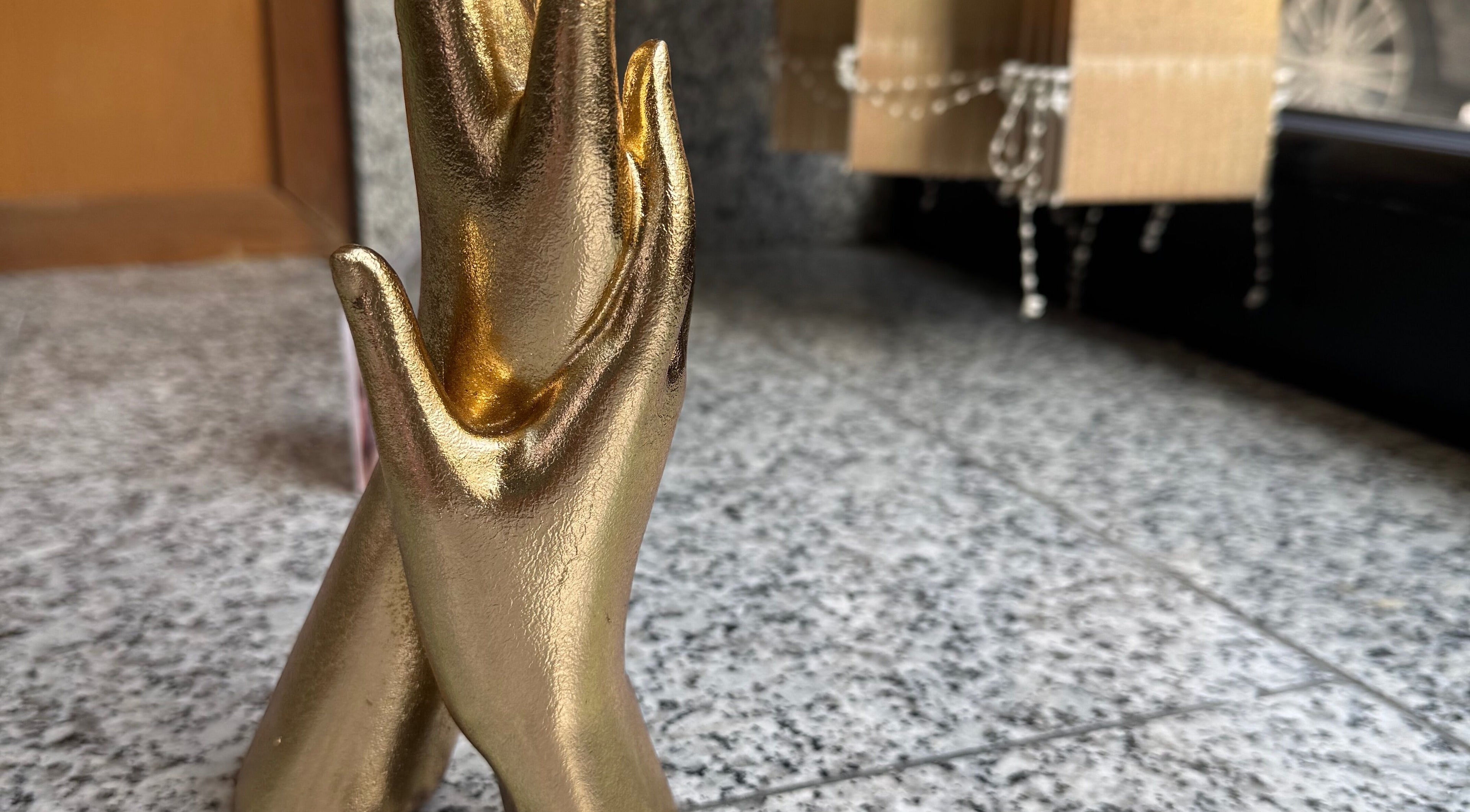 Escultura dourada de mãos entrelaçadas em Karen Passos, Algés, Lisboa, PT.