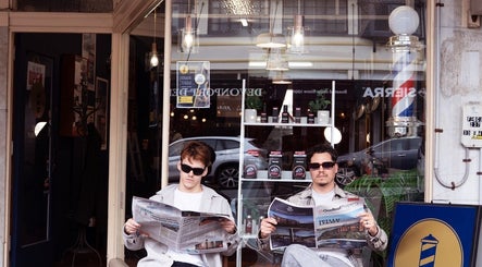 Two customers reading newspapers outside Indigo Barbers, Auckland, Auckland, NZ, under classic barbershop pole.