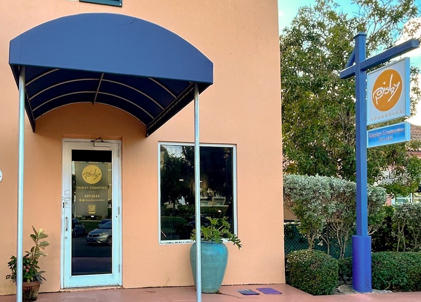 Entrance of Paisley Cosmetics in Nassau, New Providence, BS with blue canopy and potted plants.