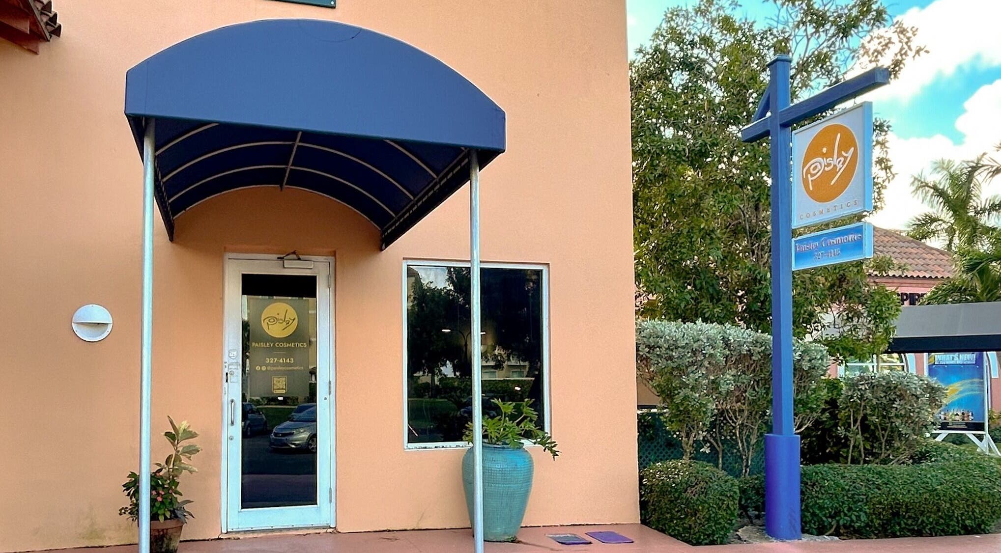 Entrance of Paisley Cosmetics in Nassau, New Providence, BS with blue canopy and potted plants.