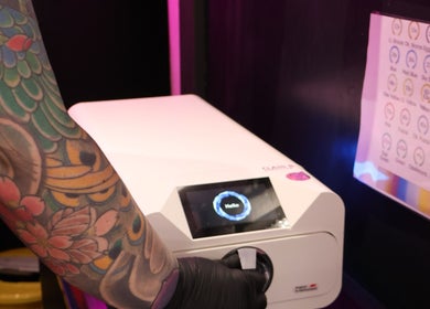 Tattooed arm operating a device at Pierce Me Jessi B in Newark-on-trent, England, GB, highlighting vibrant studio vibe.