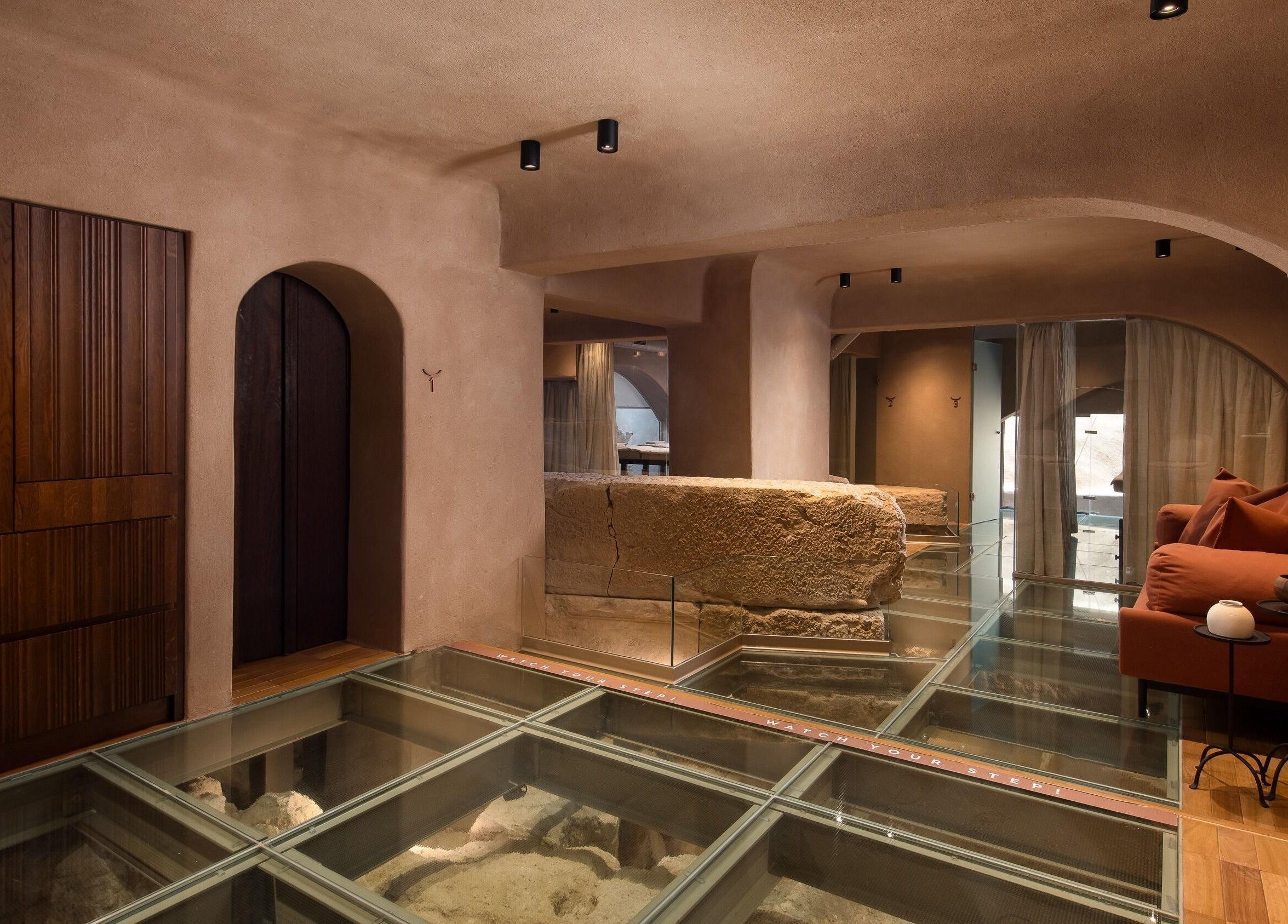Modern spa lounge at Niche Spa 300 B.C., Athina, GR, features ancient stone and glass floor exhibits.