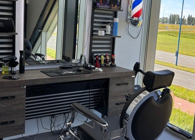 Stijlvolle kappersstoel en werkplek bij Dimma The Barber in Zoetermeer, Zuid-holland, NL met uitzicht op een groene weg.