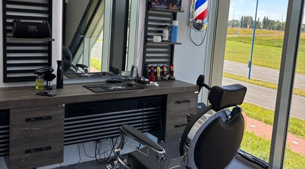 Stijlvolle kappersstoel en werkplek bij Dimma The Barber in Zoetermeer, Zuid-holland, NL met uitzicht op een groene weg.