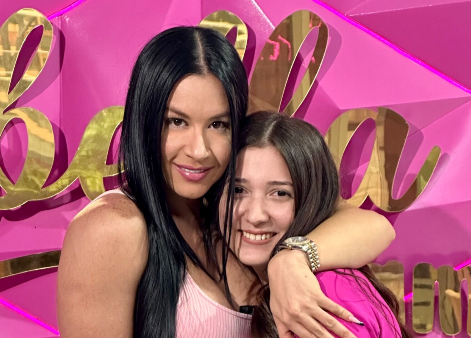 Dos mujeres sonrientes en Qbellachama Las Condes, Región Metropolitana, CL, frente a un fondo rosa vibrante.