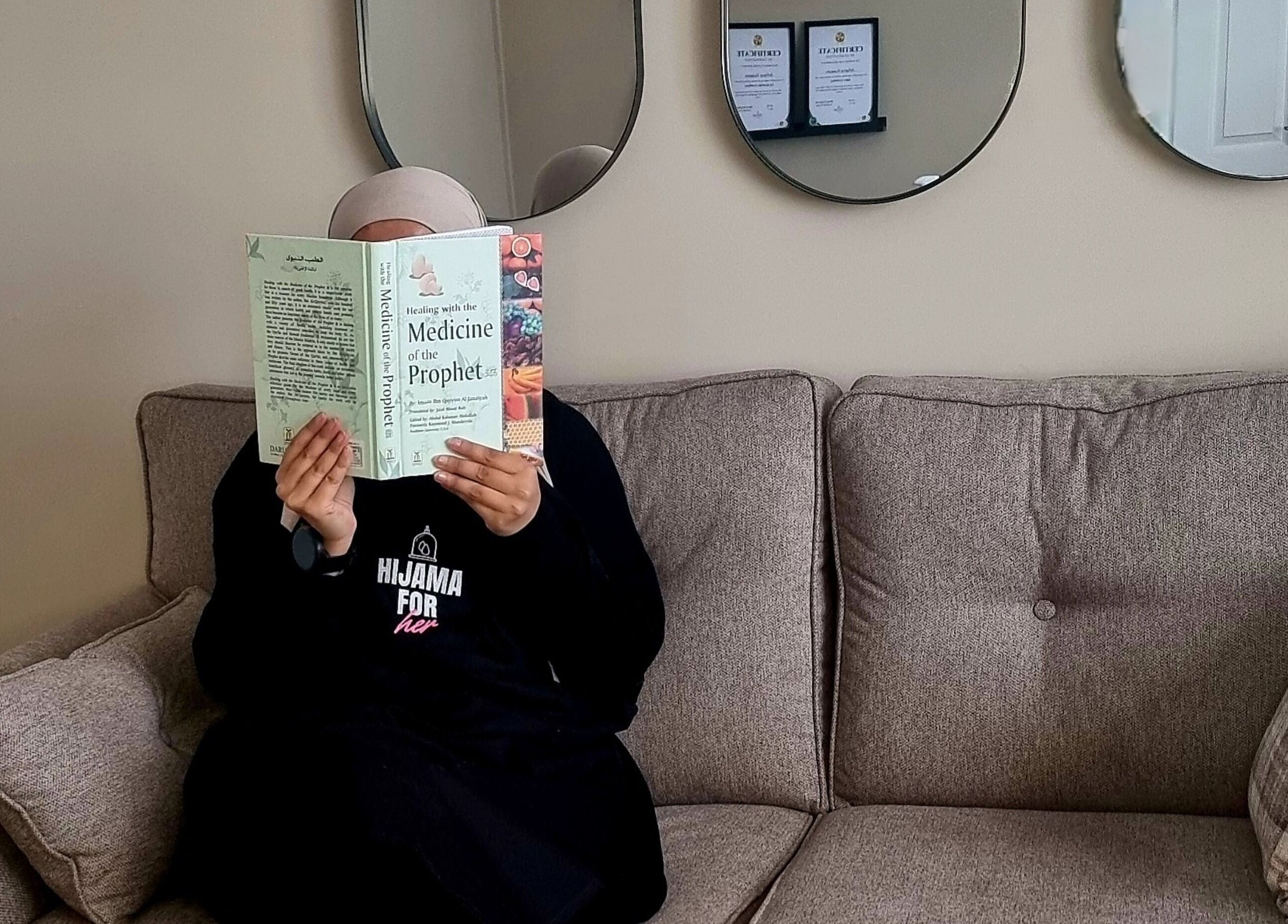 Person reading a book in Hijama for Her, Tipton, England, GB, with mirrors and certificates on the wall.