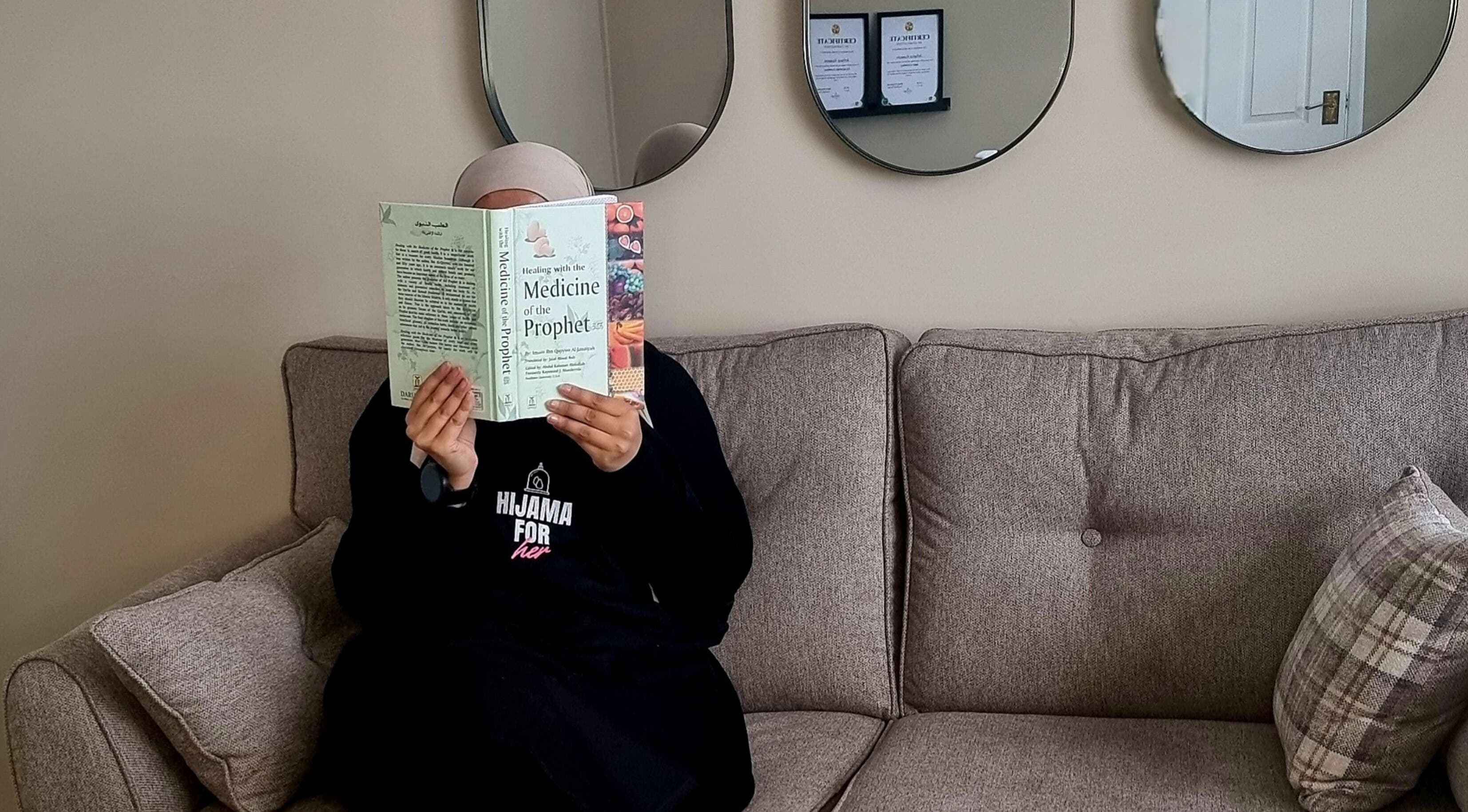 Person reading a book in Hijama for Her, Tipton, England, GB, with mirrors and certificates on the wall.