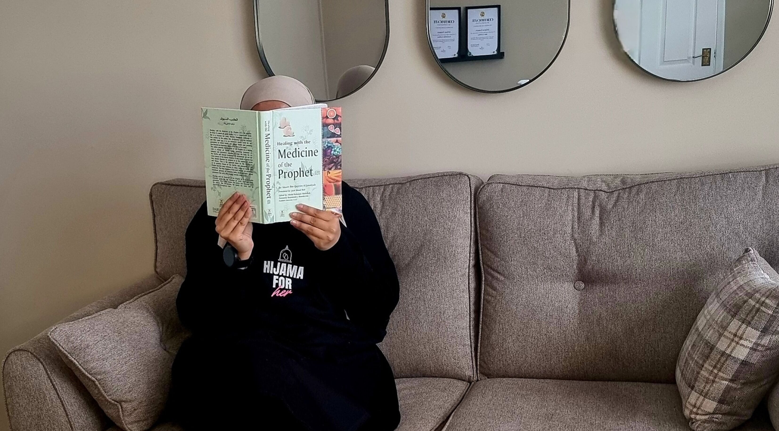 Person reading a book in Hijama for Her, Tipton, England, GB, with mirrors and certificates on the wall.