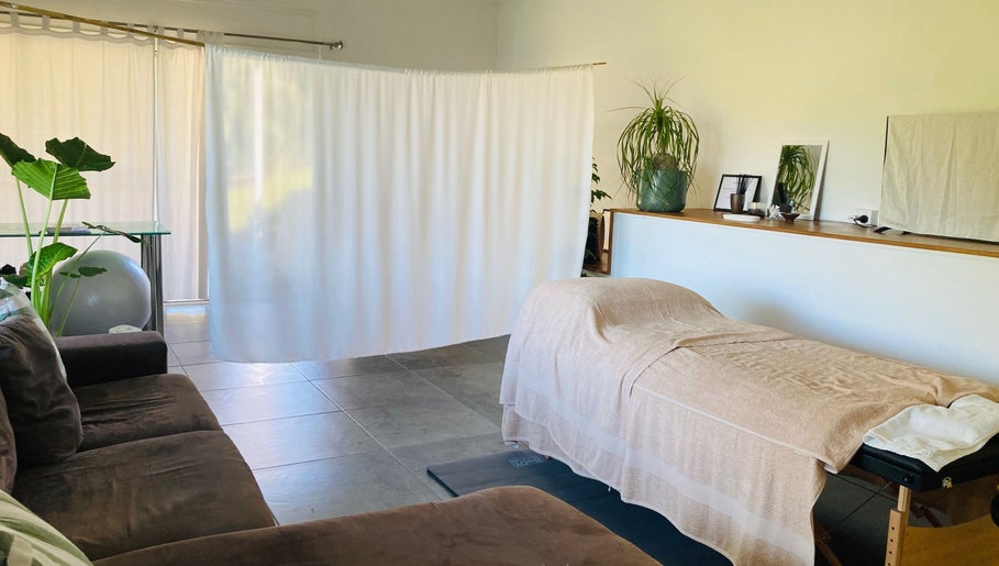 Serene massage room at Kea Forest in Korora, New South Wales, AU, featuring a cozy table and lush plants.