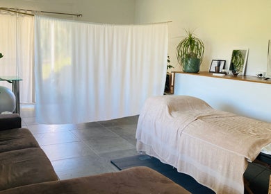 Serene massage room at Kea Forest in Korora, New South Wales, AU, featuring a cozy table and lush plants.