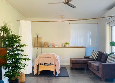 Cozy therapy room at Kea Forest in Korora, New South Wales, AU with massage table, plants, and sofa.