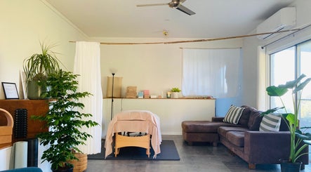 Cozy therapy room at Kea Forest in Korora, New South Wales, AU with massage table, plants, and sofa.