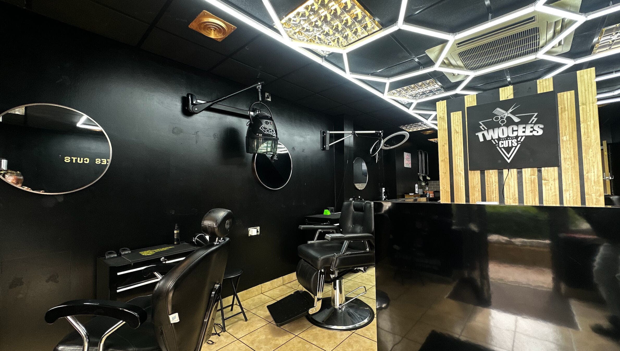 Chic black interior of Twocees Cuts salon in Stoke-on-Trent, England, GB with stylish mirrors and chairs.