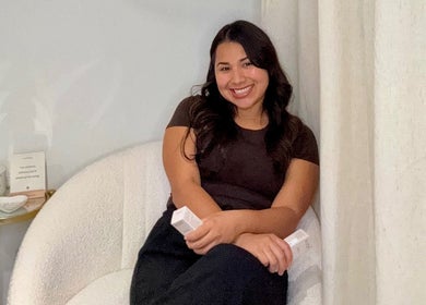 Smiling woman seated in cozy corner at Jenn’s Beauty Lounge, Kyle, Texas, US, holding beauty products.