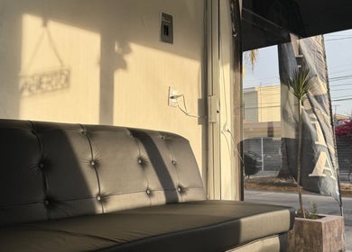 Sofá de cuero negro con luz solar en Quimera Barbershop, Tepic, Nayarit, MX.