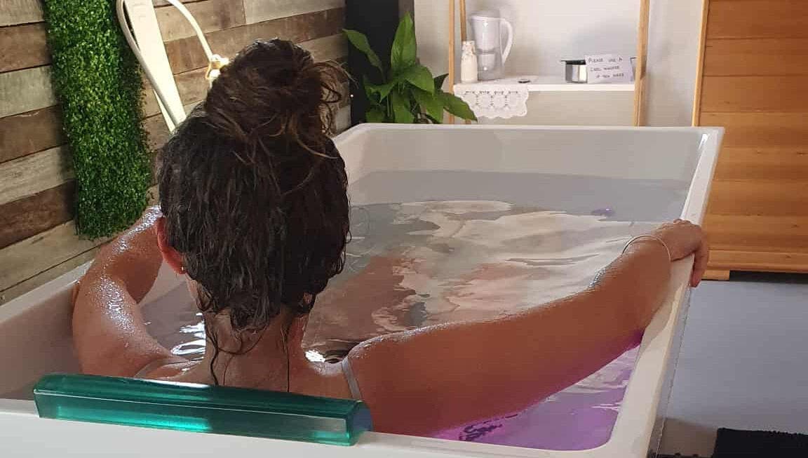 A person relaxes in a spa bath at The Grounding Room, Chatsworth, Queensland, AU, surrounded by greenery.