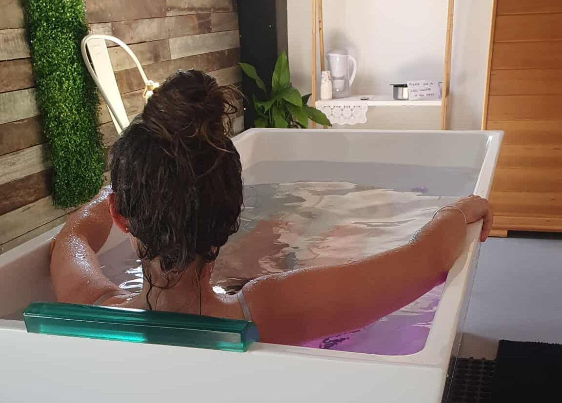 A person relaxes in a spa bath at The Grounding Room, Chatsworth, Queensland, AU, surrounded by greenery.
