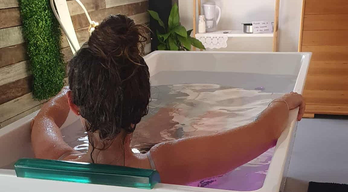 A person relaxes in a spa bath at The Grounding Room, Chatsworth, Queensland, AU, surrounded by greenery.