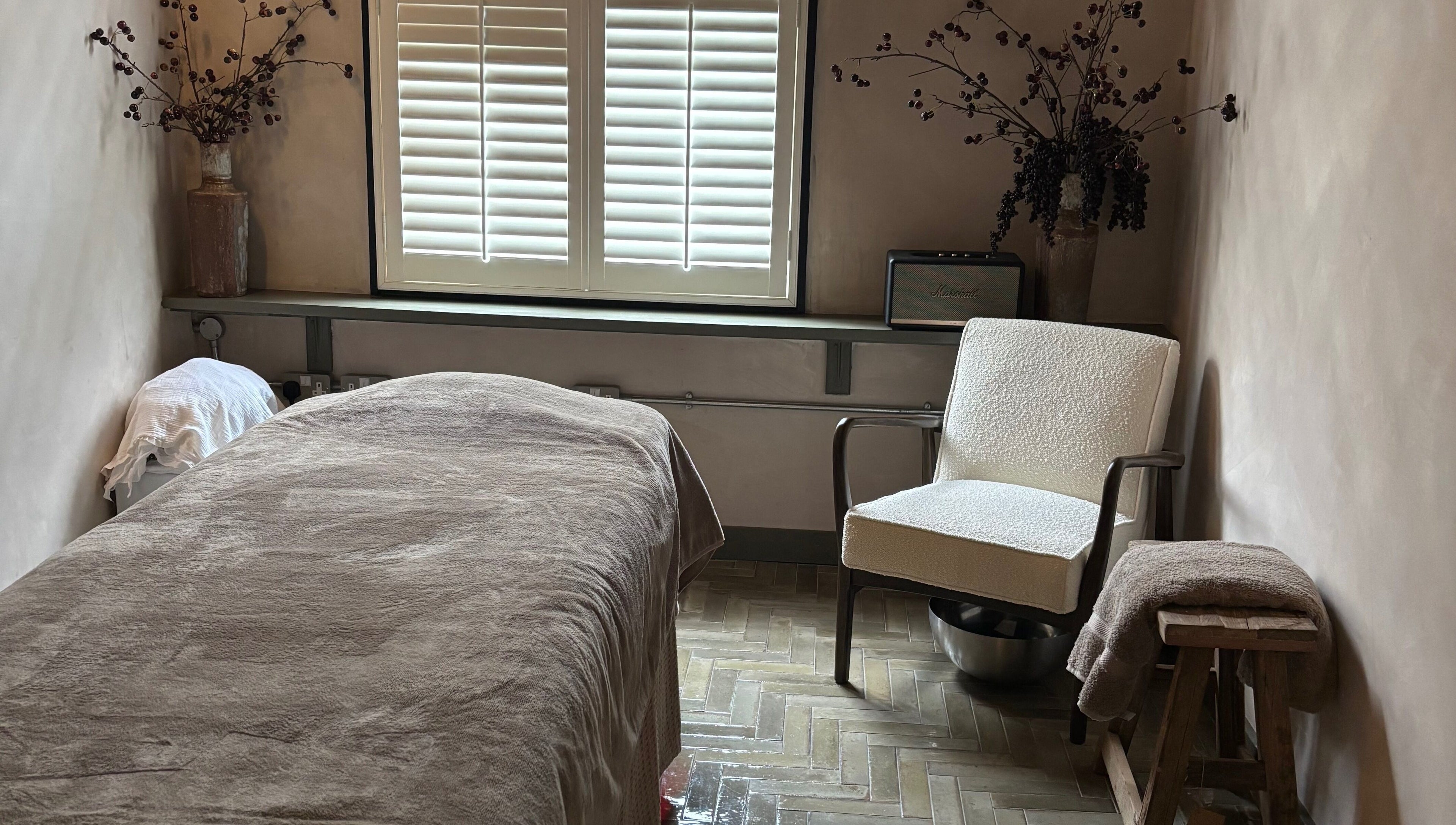 Cozy treatment room at Elaine Sadler Skin Health, Warwick, England, GB with a bed, chair, and soft lighting.