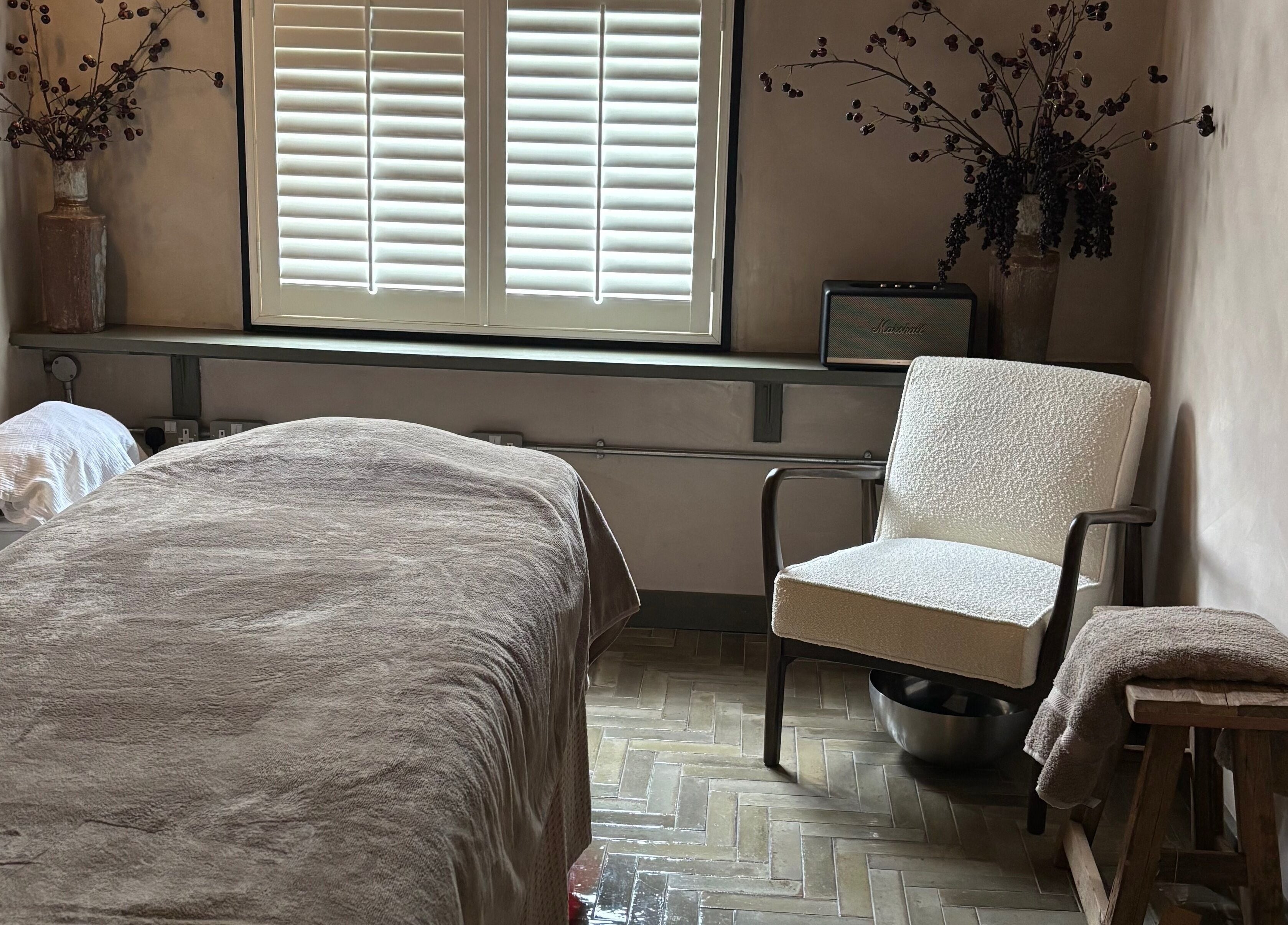 Cozy treatment room at Elaine Sadler Skin Health, Warwick, England, GB with a bed, chair, and soft lighting.
