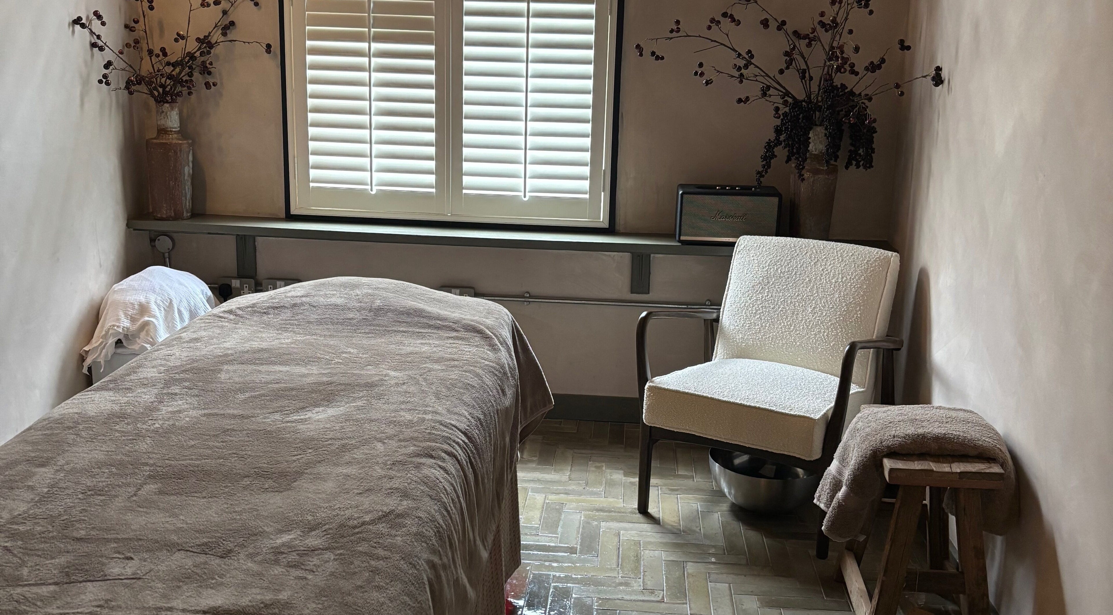 Cozy treatment room at Elaine Sadler Skin Health, Warwick, England, GB with a bed, chair, and soft lighting.