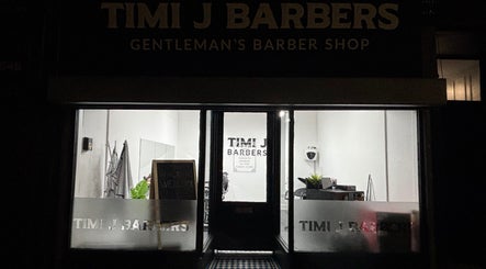 Entrance of TIMI J BARBERS in Paisley, Scotland, GB, warmly lit at night with welcoming decor.