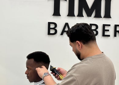 Barber at TIMI J BARBERS in Paisley, Scotland, GB, expertly trims a client's hair.