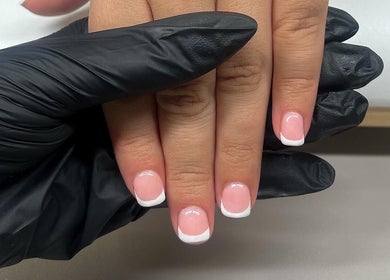 Elegant French manicure at Nailsbybry, Ampthill, England, GB. Black gloves hold hands with pink nails featuring white tips.