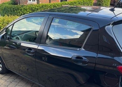 Sleek black car parked at NJCleaningCo in St Albans, GB, showcasing reflection of vibrant surroundings.