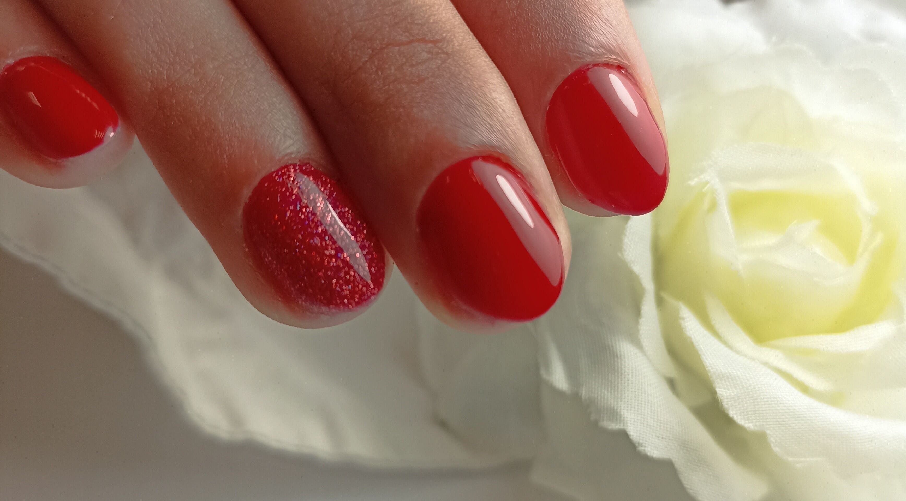 Manucure rouge élégante à Aline, Mer, Centre-val De Loire, FR, avec une fleur blanche en arrière-plan.