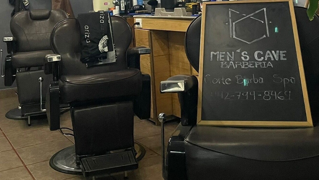 Interior de Barbería Men's Cave en El Pueblito, Querétaro, MX, con sillas de cuero y pizarra de servicios.