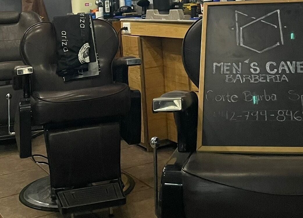 Interior de Barbería Men's Cave en El Pueblito, Querétaro, MX, con sillas de cuero y pizarra de servicios.
