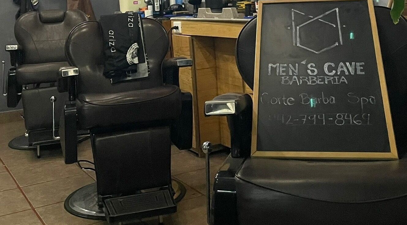 Interior de Barbería Men's Cave en El Pueblito, Querétaro, MX, con sillas de cuero y pizarra de servicios.