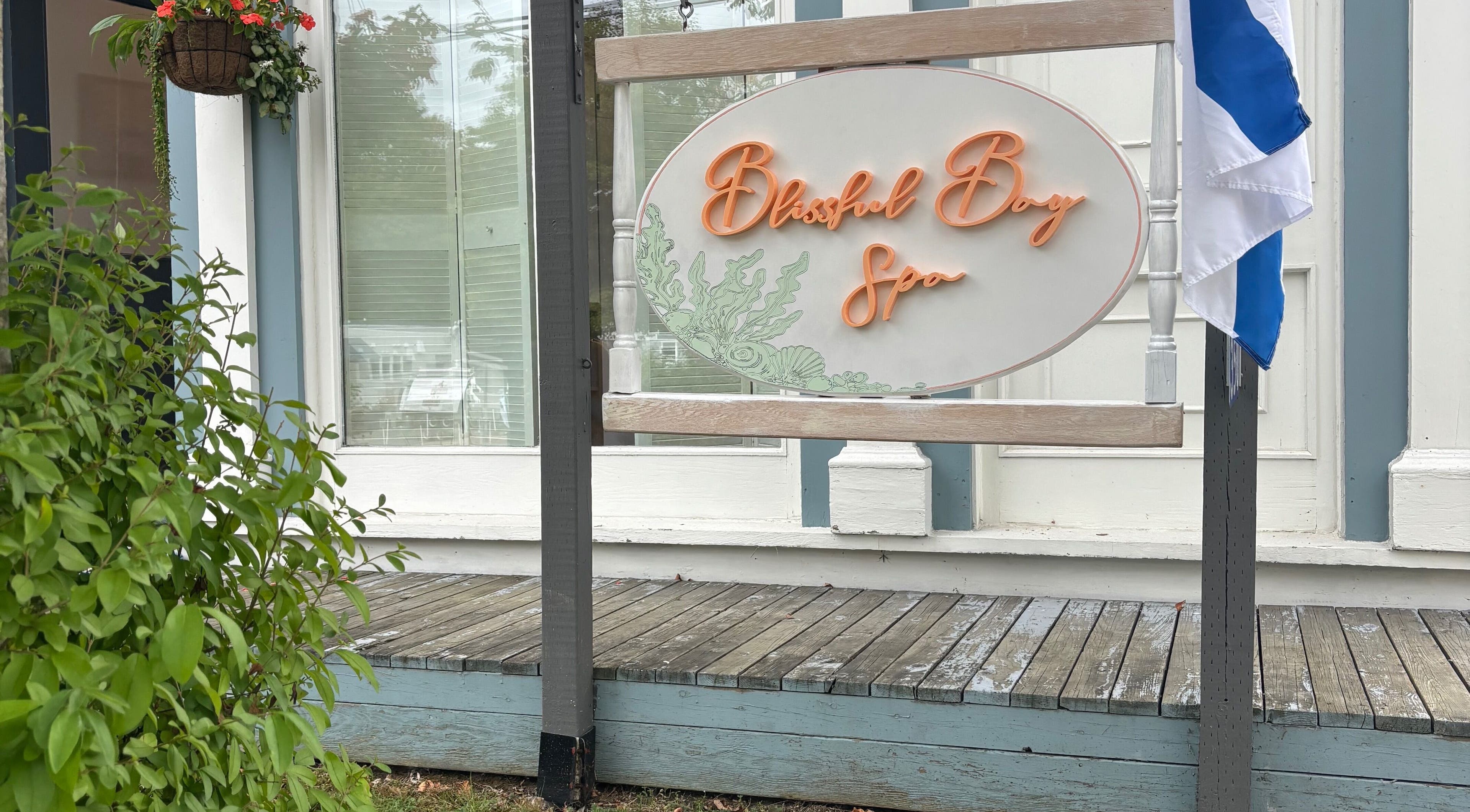 Sign of Blissful Bay Spa with Jennie amidst greenery in Mahone Bay, Nova Scotia, CA, inviting relaxation.