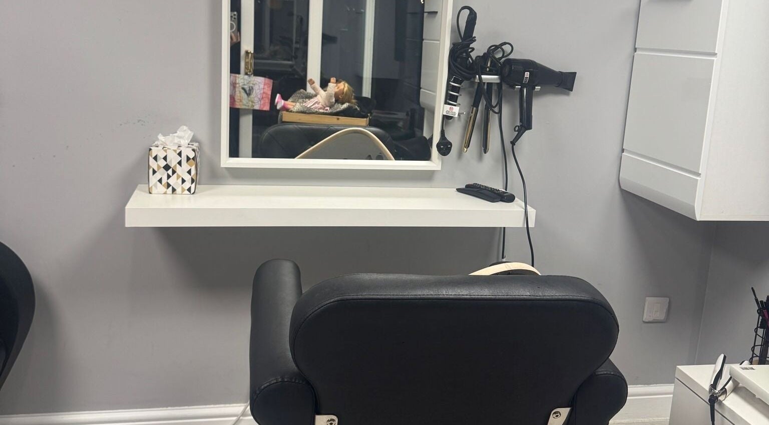 Modern salon setup at Mila Hair Atelier, Epsom, England, GB, featuring a black styling chair and elegant mirror.