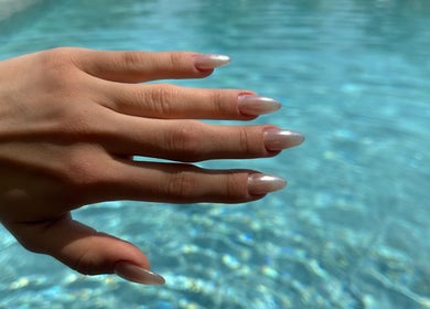 Elegant manicured hand by Angel Nails, Uccle, Bruxelles, BE, with a serene pool backdrop.