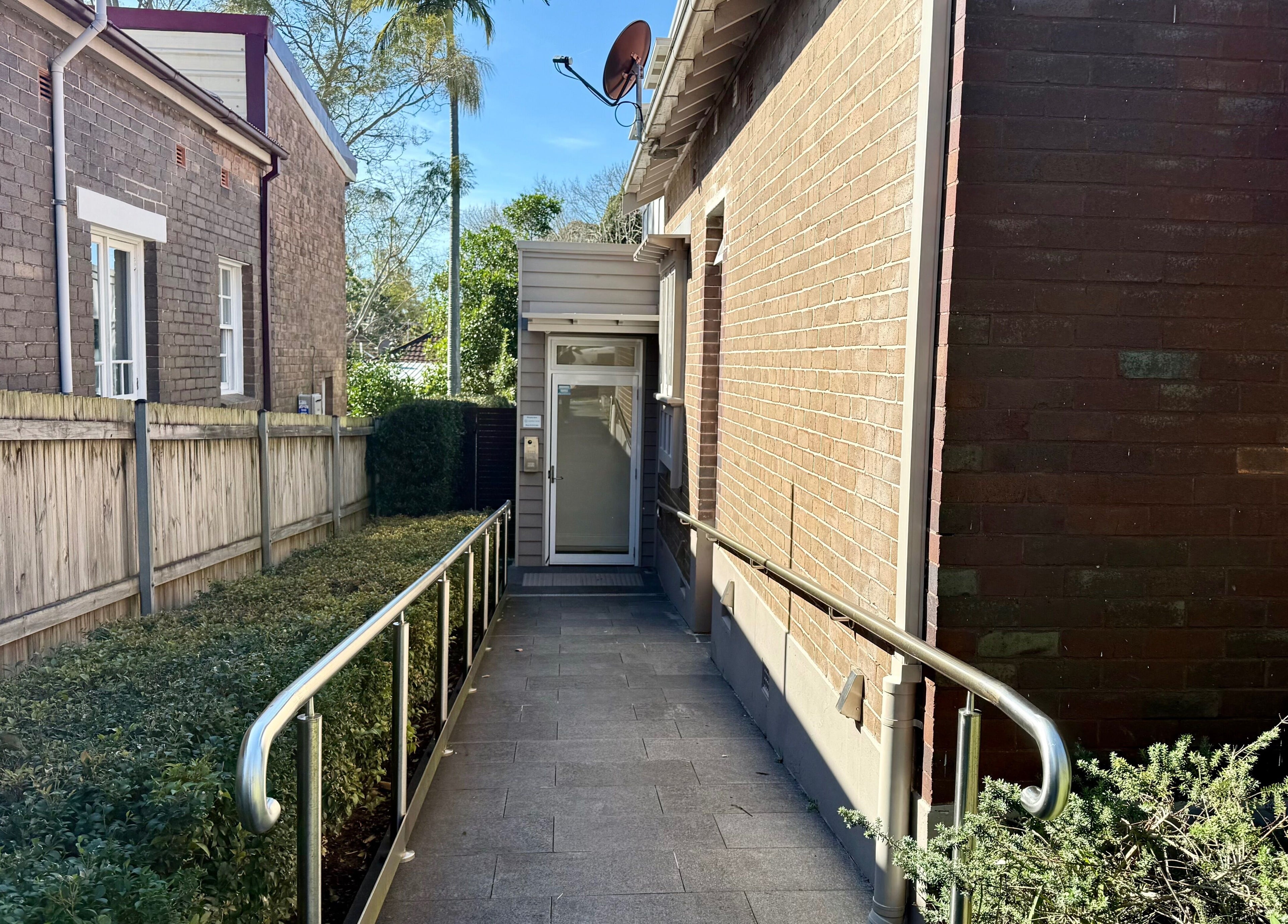 Entrance pathway to Ember Lash, Lilyfield, New South Wales, AU, with a lush garden and brick exterior.