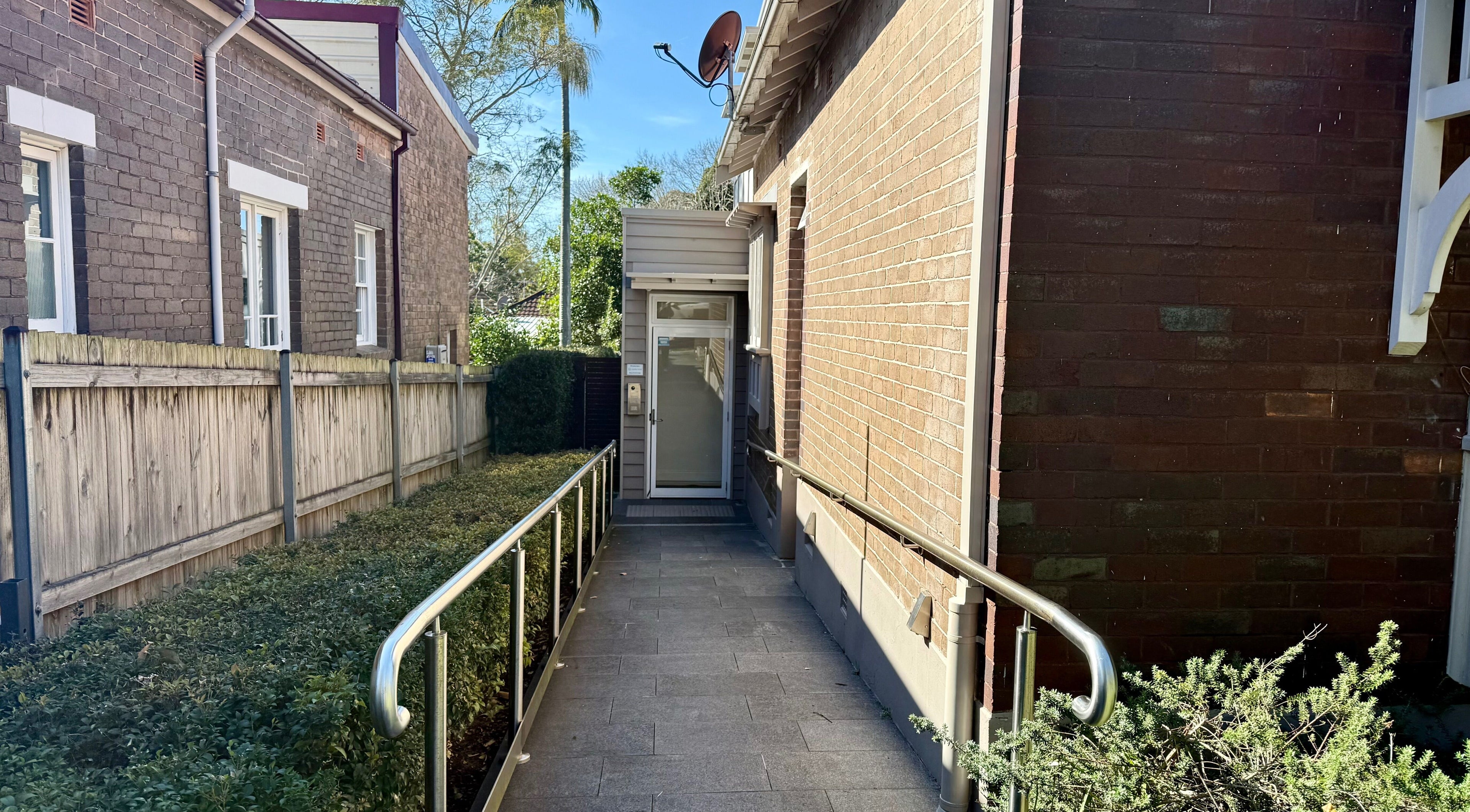 Entrance pathway to Ember Lash, Lilyfield, New South Wales, AU, with a lush garden and brick exterior.