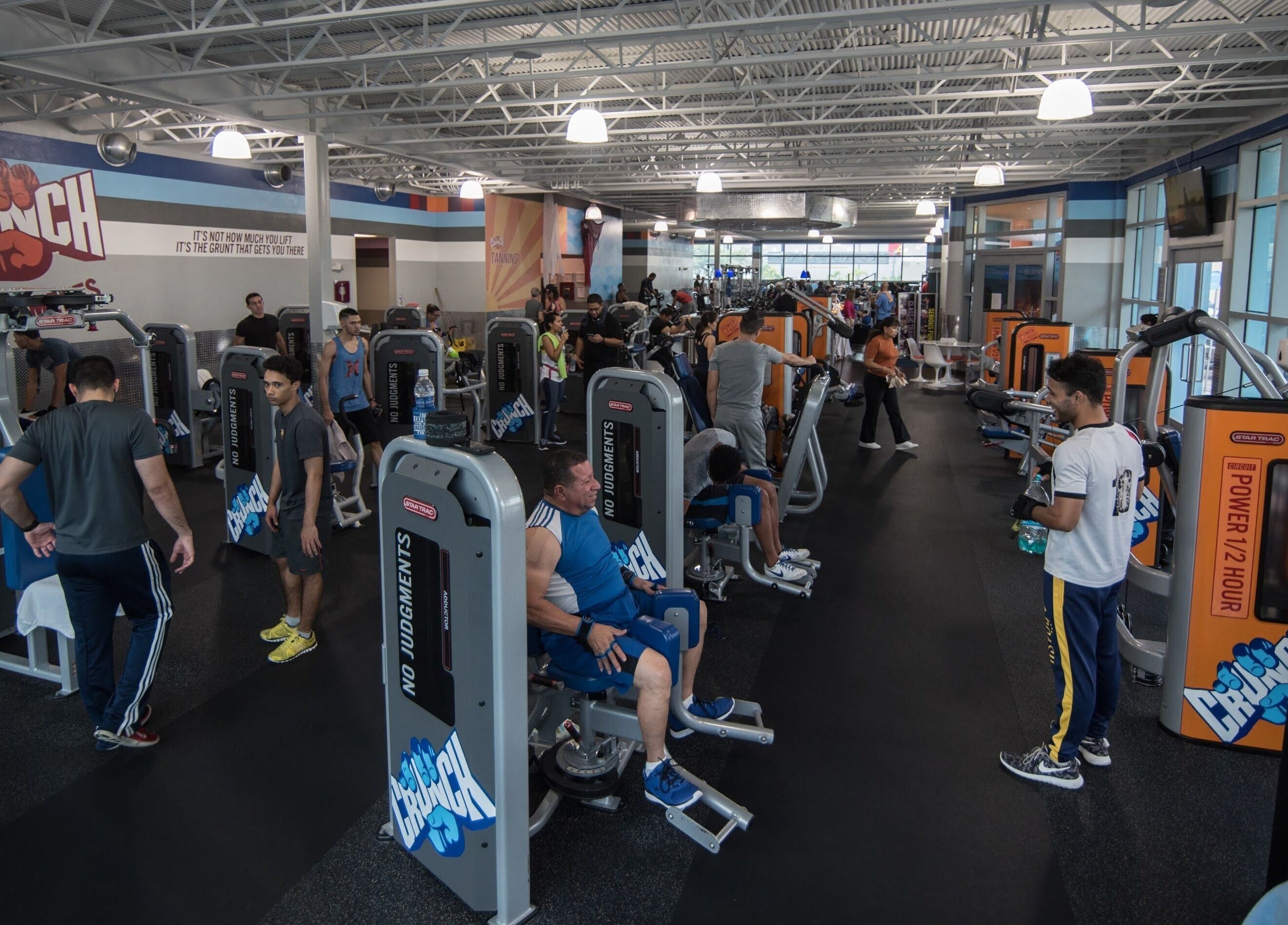 Gimnasio moderno en Crunch Fitness Carolina, Carolina, PR con personas usando máquinas de ejercicio.