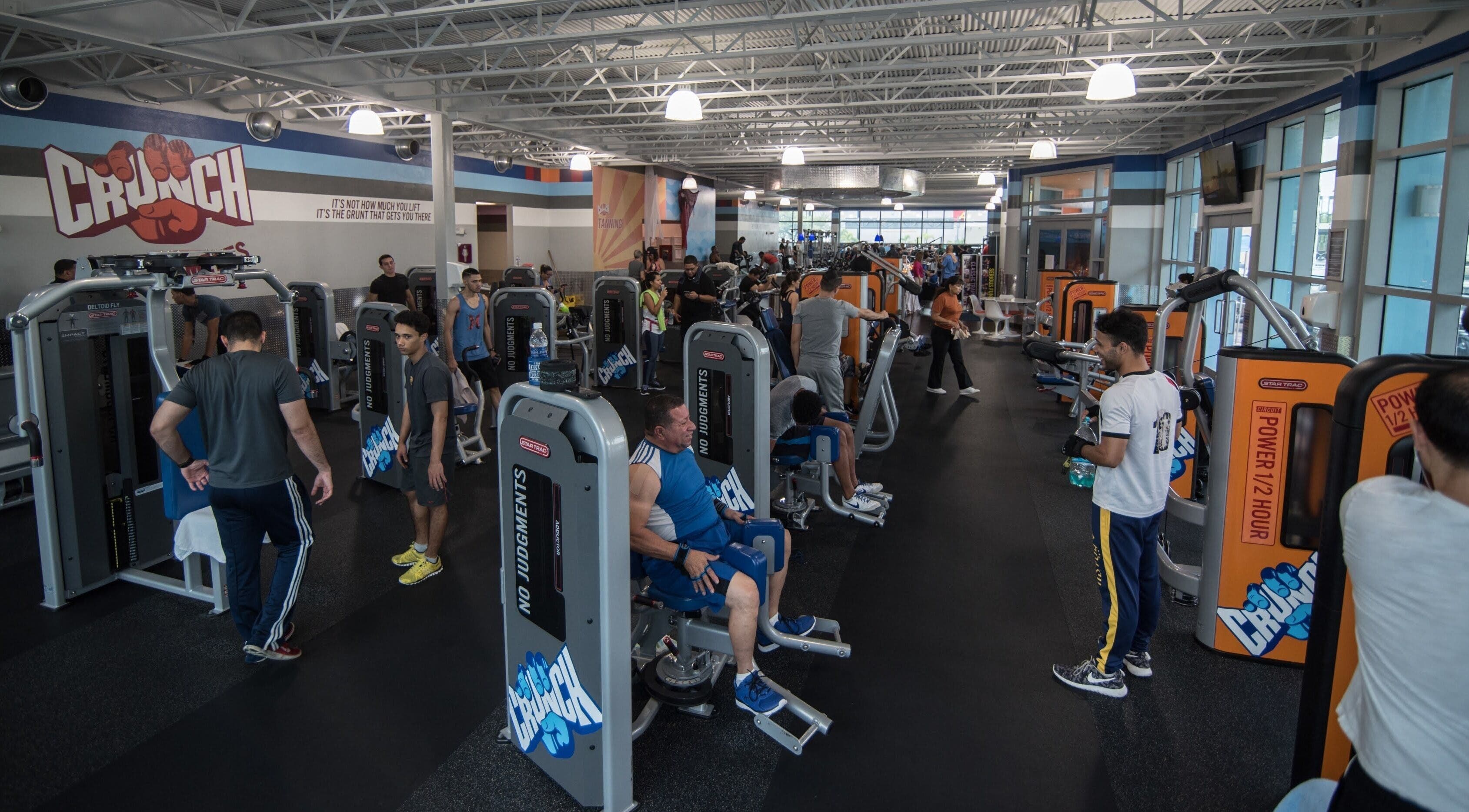 Gimnasio moderno en Crunch Fitness Carolina, Carolina, PR con personas usando máquinas de ejercicio.