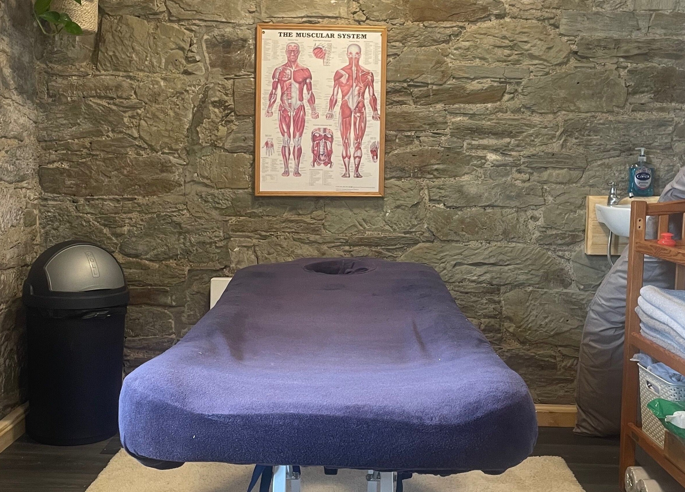 Cozy massage room at Marie’s Sports and Wellbeing Massage in Porthleven, England, GB with a stone wall decor.