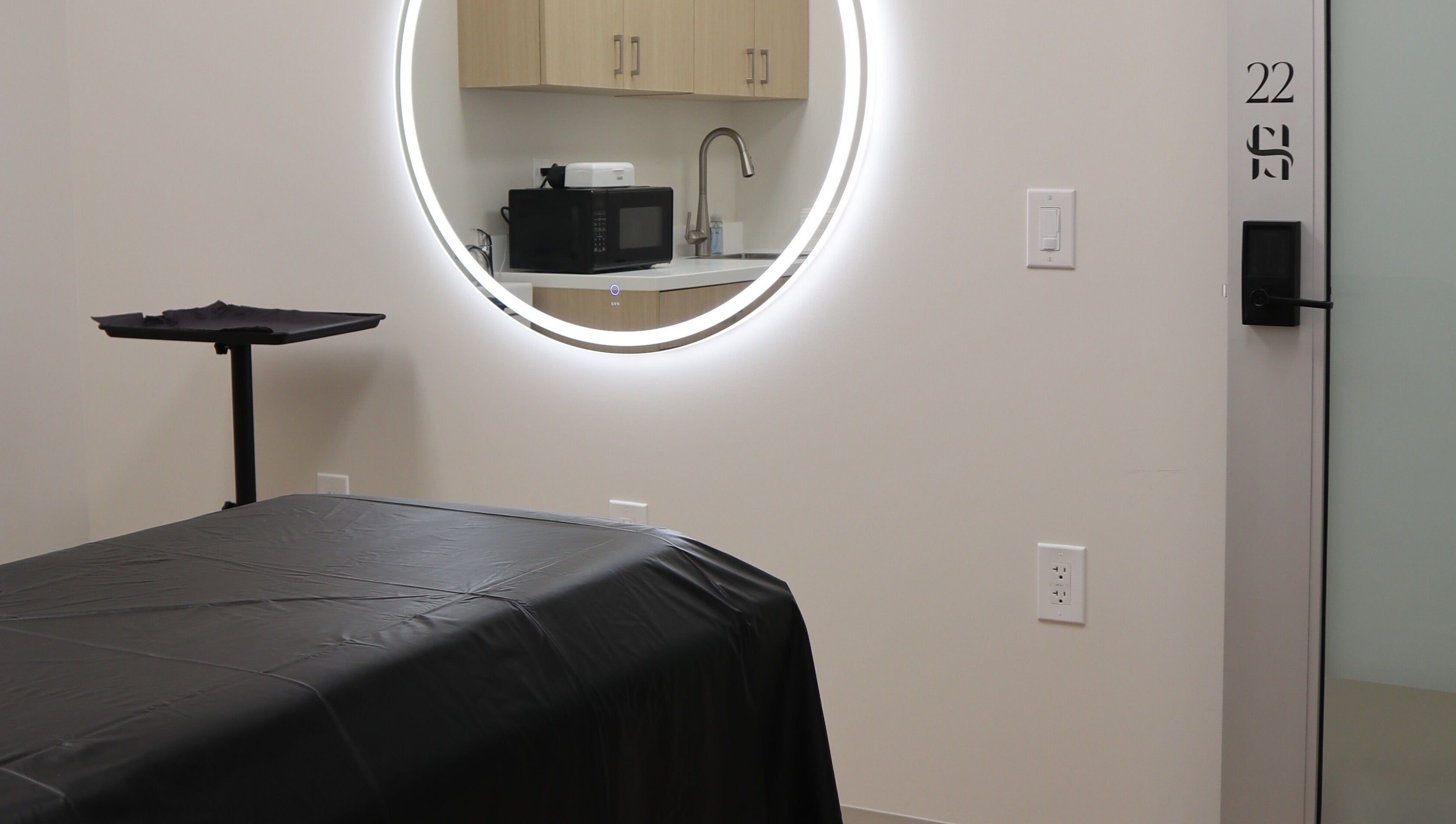Modern treatment room at DIVINE DERMABAR, Toronto, Ontario, CA with circular mirror and sleek decor.