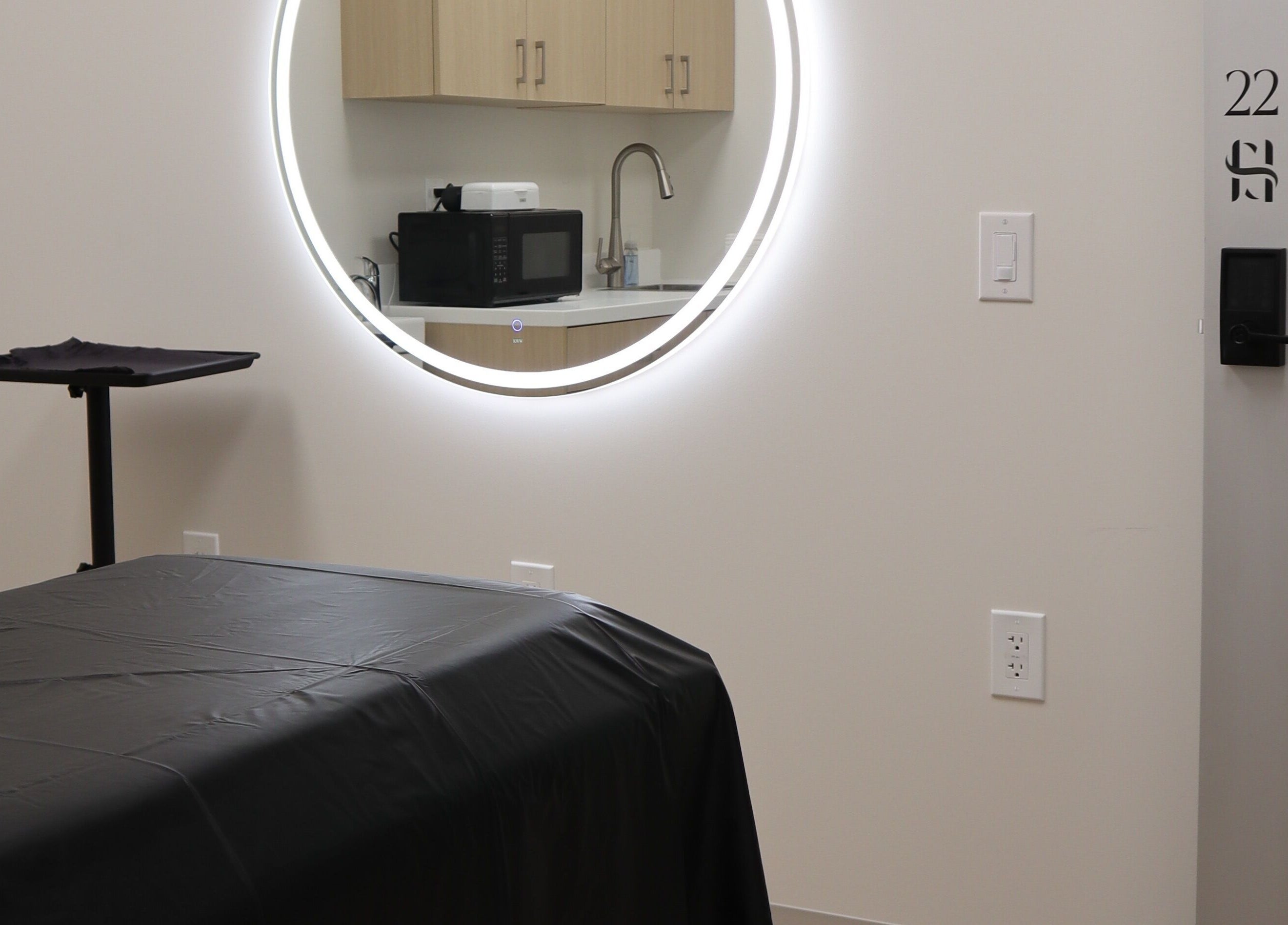 Modern treatment room at DIVINE DERMABAR, Toronto, Ontario, CA with circular mirror and sleek decor.