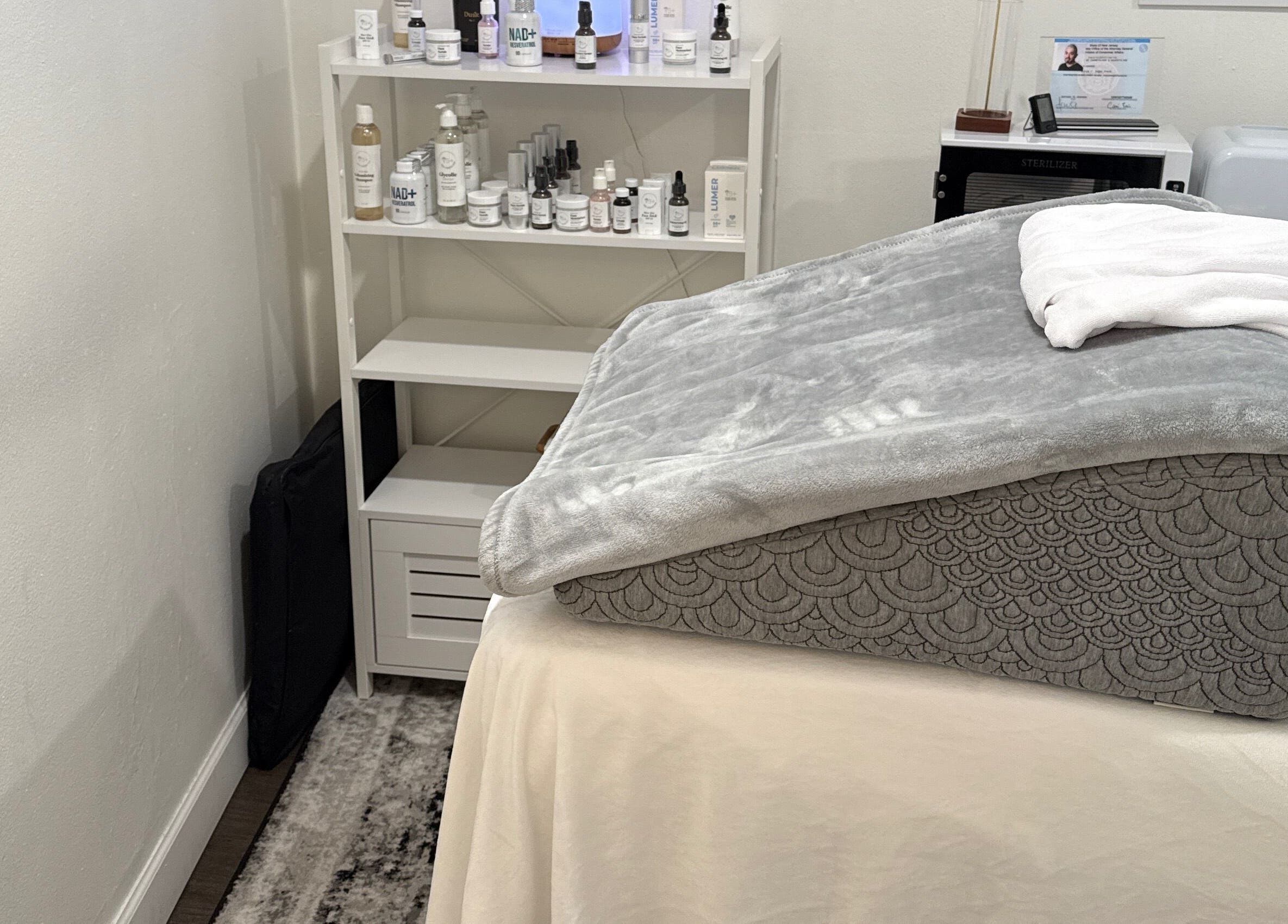 Sala de tratamiento en Your Skincare Plus, Garfield, New Jersey, US, mostrando una camilla con manta gris.