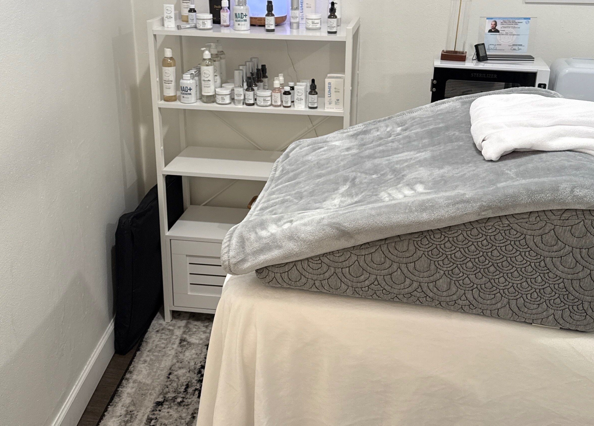 Sala de tratamiento en Your Skincare Plus, Garfield, New Jersey, US, mostrando una camilla con manta gris.