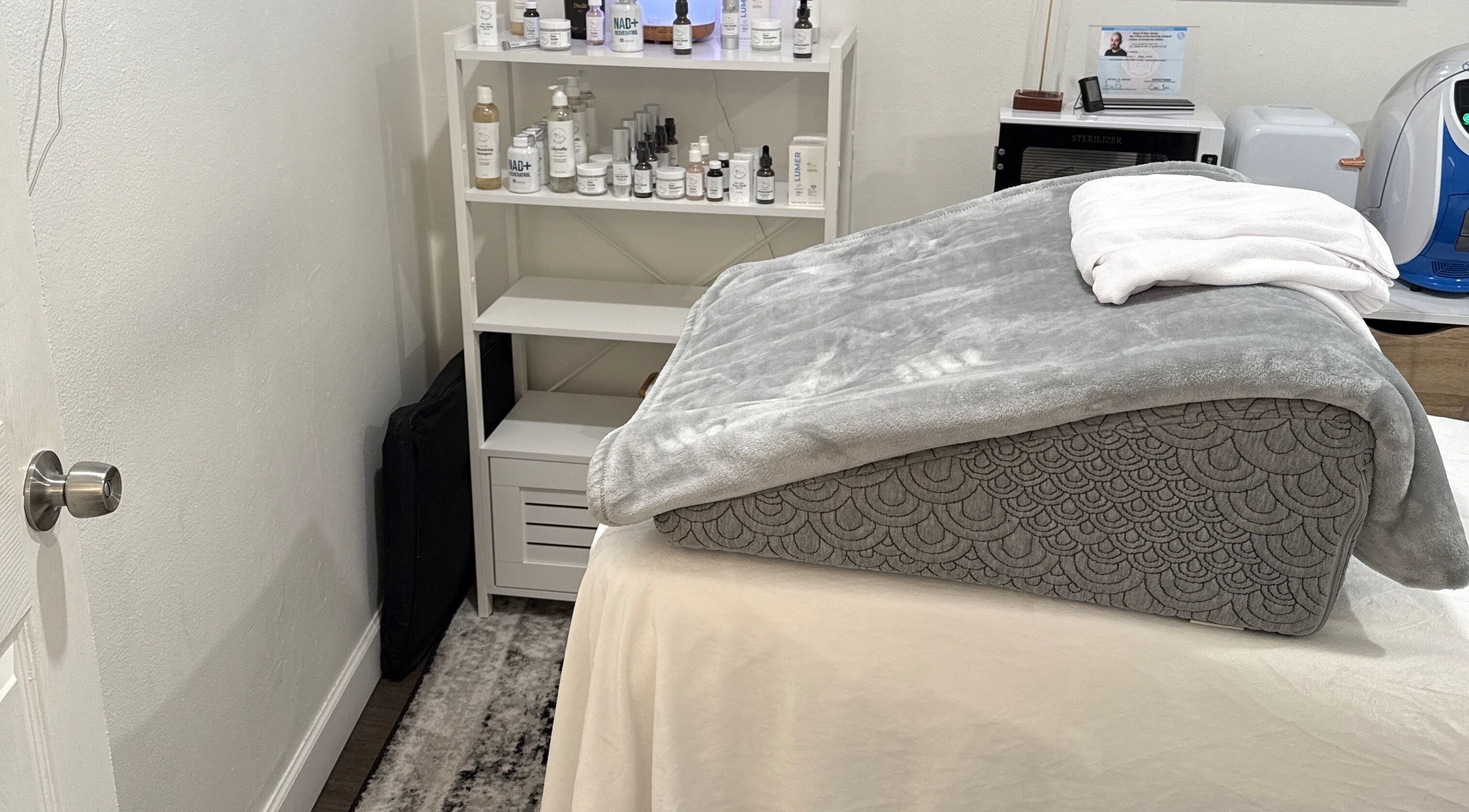 Sala de tratamiento en Your Skincare Plus, Garfield, New Jersey, US, mostrando una camilla con manta gris.