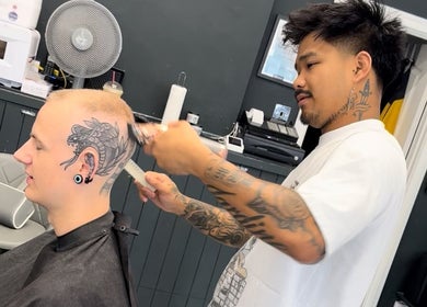 Talent at S.B.T Impact Barbers in Old Sarum, England, GB, tattooed stylist expertly trims client's hair.