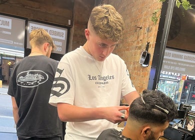 Stylist at S.B.T Impact Barbers, Old Sarum, England, GB, skillfully trims a client's hair in a modern salon setting.
