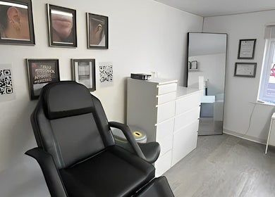 Piercing studio at Anya Celyn Piercings, Amlwch, Wales, GB, featuring a black chair and framed artwork.