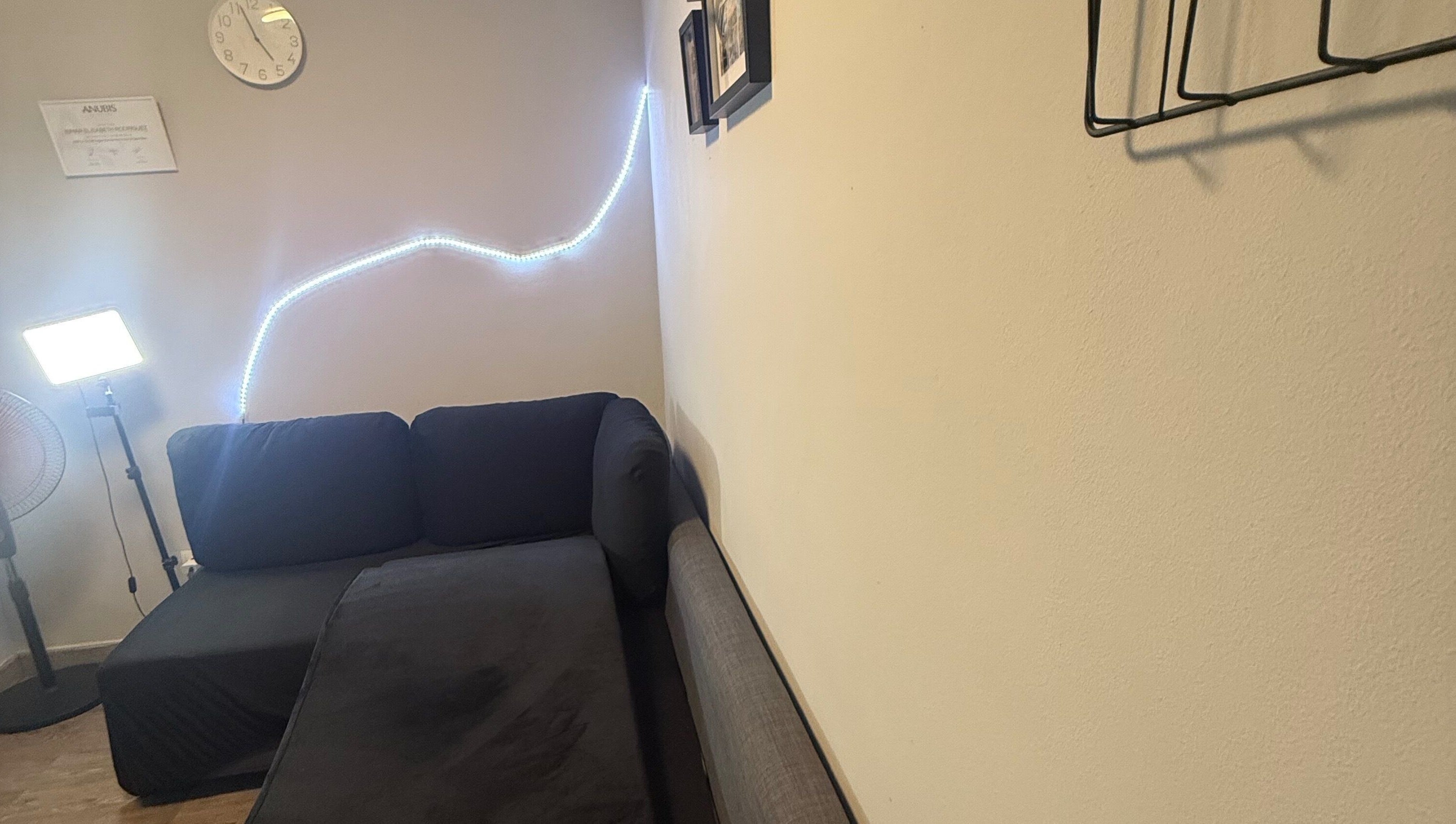 Sala acogedora en Kyiscejas, Barcelona, Catalunya, ES, con sofá negro y luz LED ambiental en la pared.